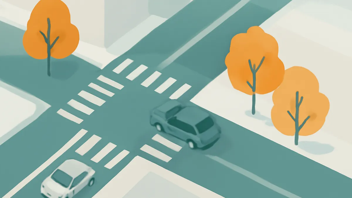 An overhead view of a car at a crosswalk and another car approaching an intersection, with trees nearby