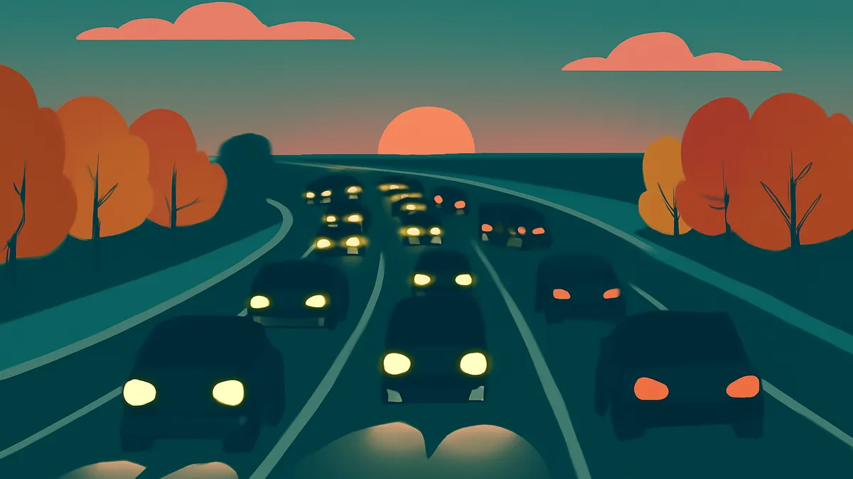 A highway at sunset with many cars driving, their headlights and taillights glowing, and trees on the side