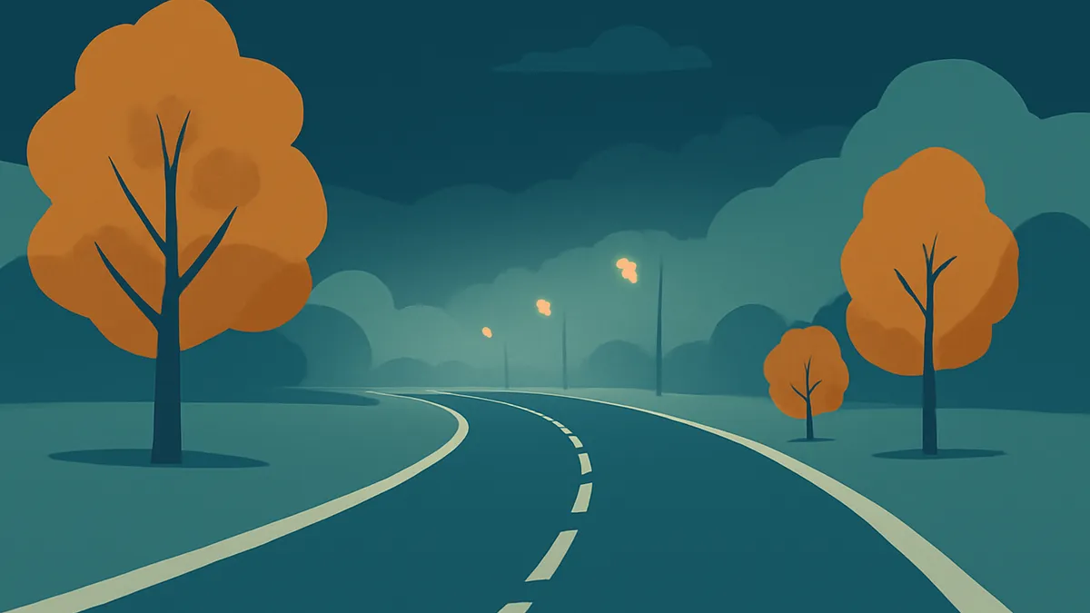 A winding road at night with streetlights and trees with orange leaves under a dark sky
